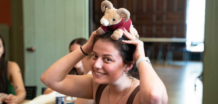 photo of mel hills holding a stuffed toy doll of ramses, fordham's mascot, on her head