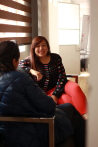 two women sit on a bench. one smiles at the other.