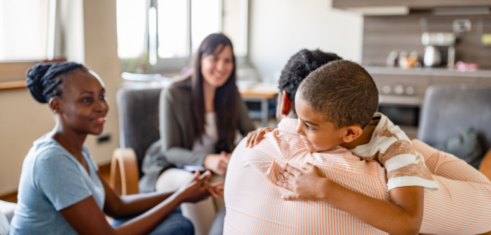 a child and adult hug while two other adults look on and smile.