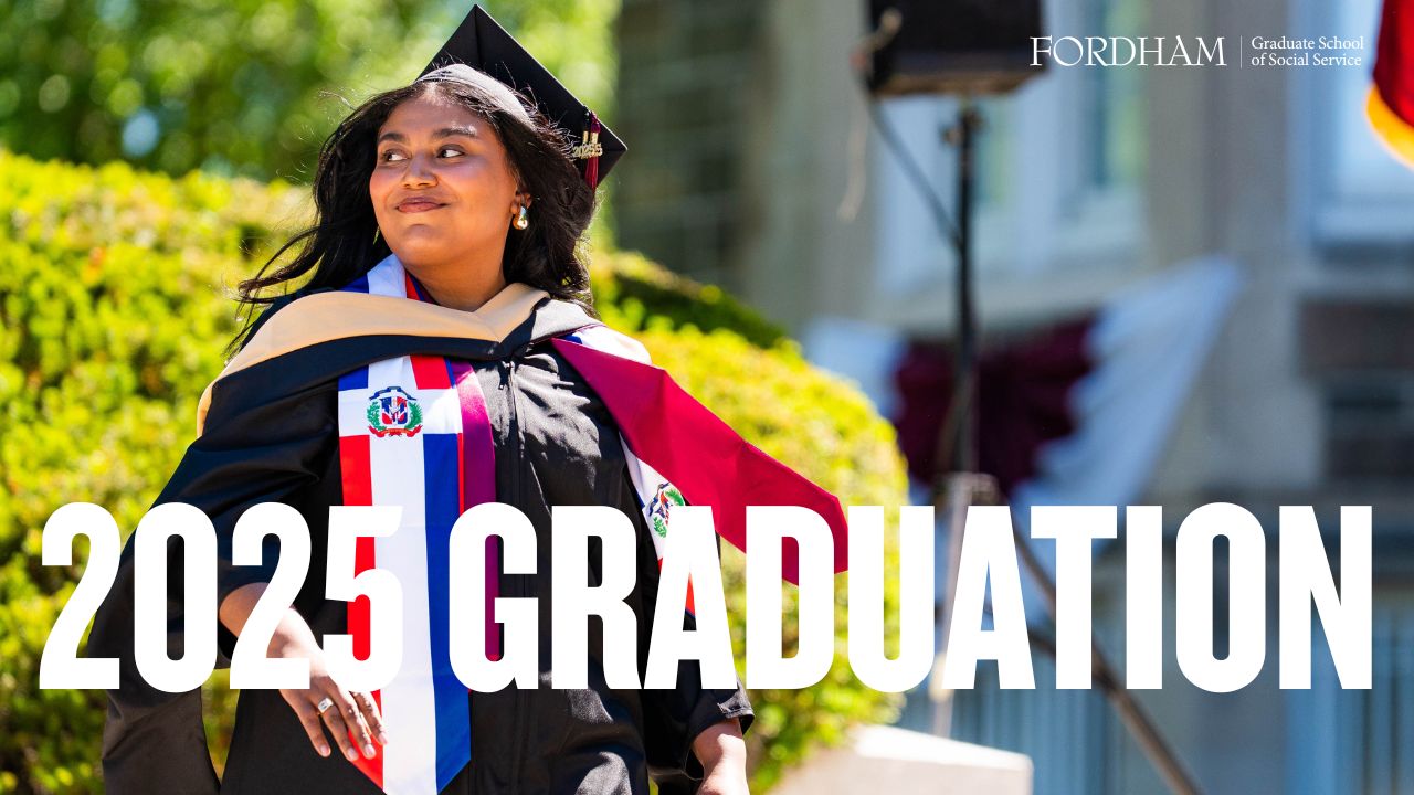 A student walks across the graduation stage, smiling at the crowd. 