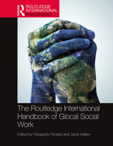 Cover of the book "The Routledge International Handbook of Glocal Social Work," edited by Panagiotis Pentaris and Janet Walker. The cover features two human hands clasped together, painted with a world map to symbolize global unity. The top banner displays the Routledge International Handbooks logo.